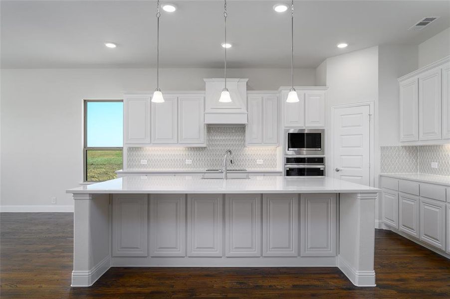 Kitchen featuring dark wood-type flooring, a kitchen island with sink, and white cabinets