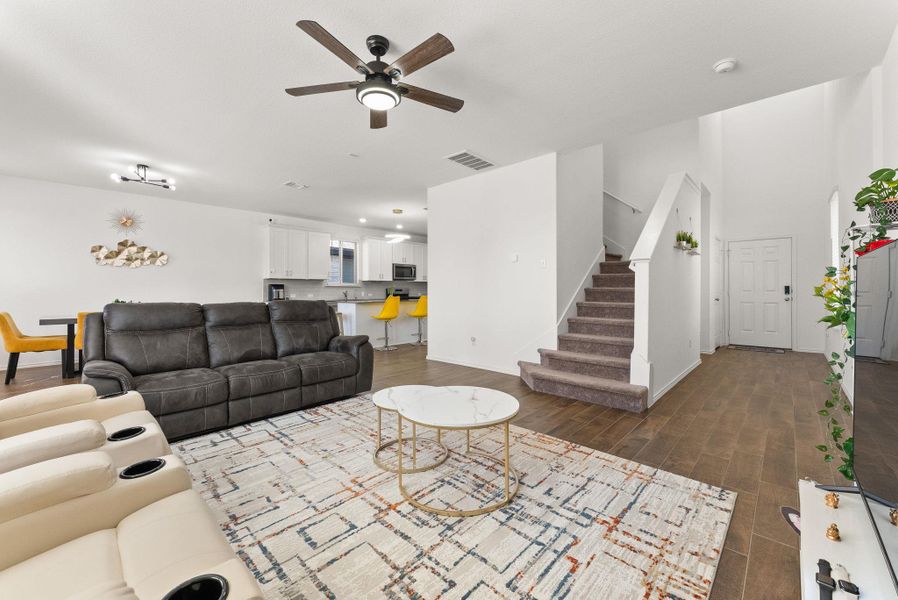 Living room with baseboards, visible vents, ceiling fan, dark wood-type flooring, and stairs