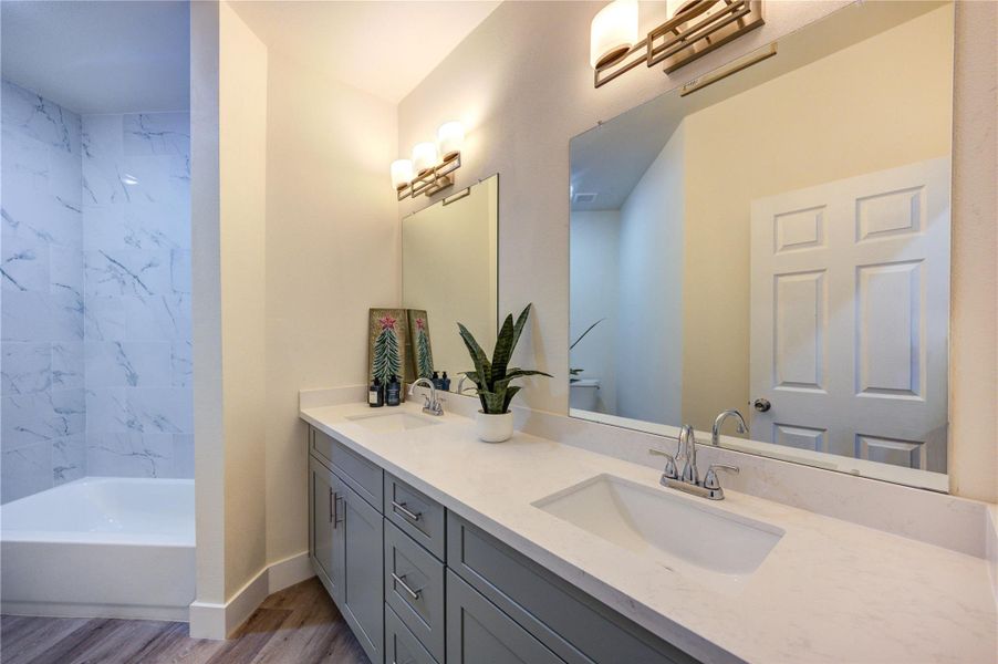 This bathroom features a modern design with a large mirror, elegant lighting, and a sleek vanity with ample storage. The shower area is accented by stylish marble-like tiles, creating a clean and inviting space.