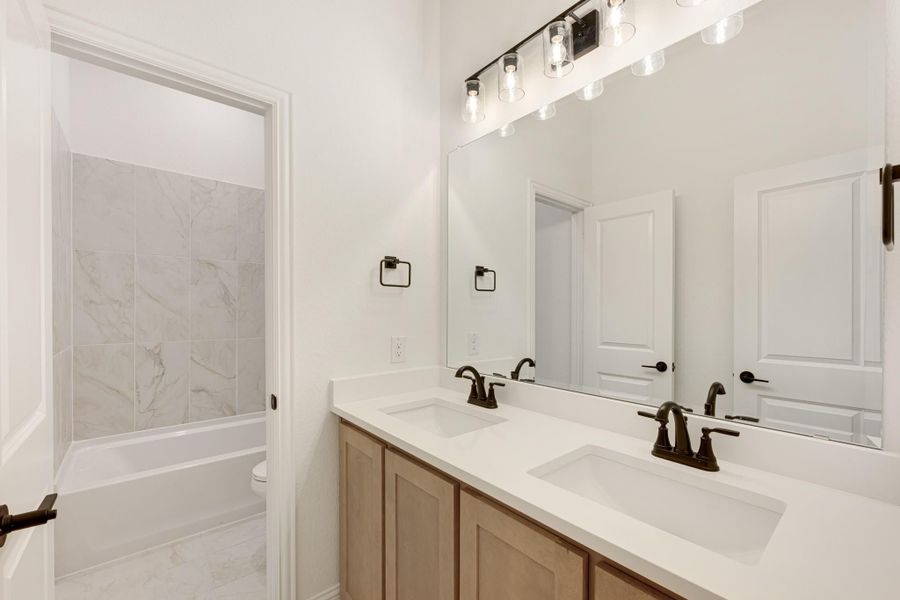 Bathroom with double sink vanity, wood cabinets, large mirror, and separate tub with marble tile surround