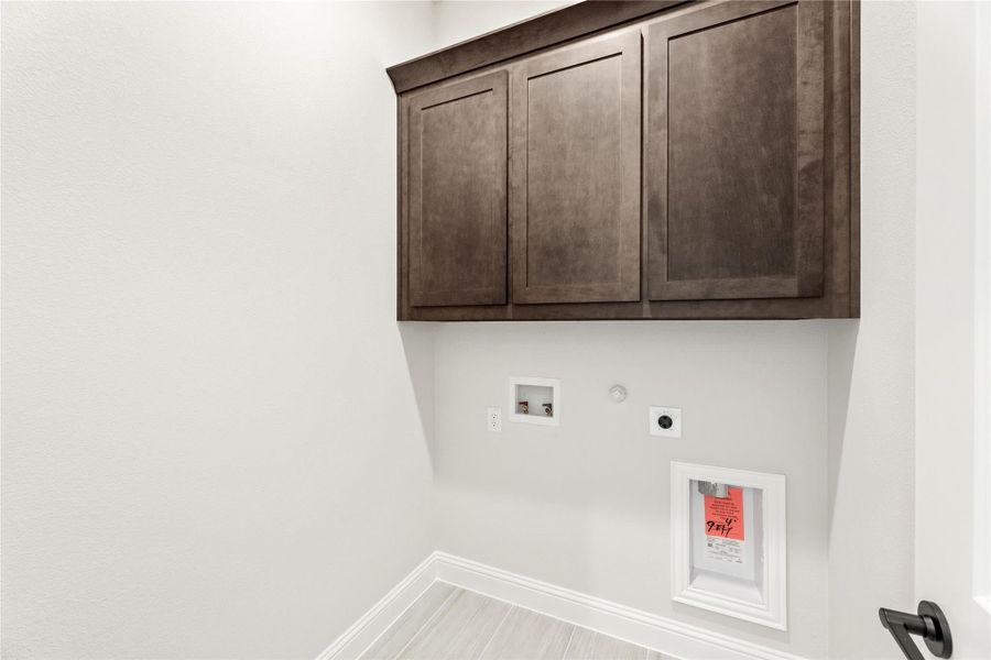 Laundry room with dark wood upper cabinets, washer and dryer hookups, and light tile flooring Laundry room with dark wood upper cabinets, washer and dryer hookups, and light tile flooring
