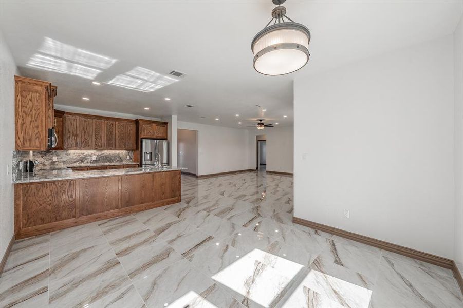 Kitchen featuring tasteful backsplash, brown cabinetry, appliances with stainless steel finishes, open floor plan, and a peninsula