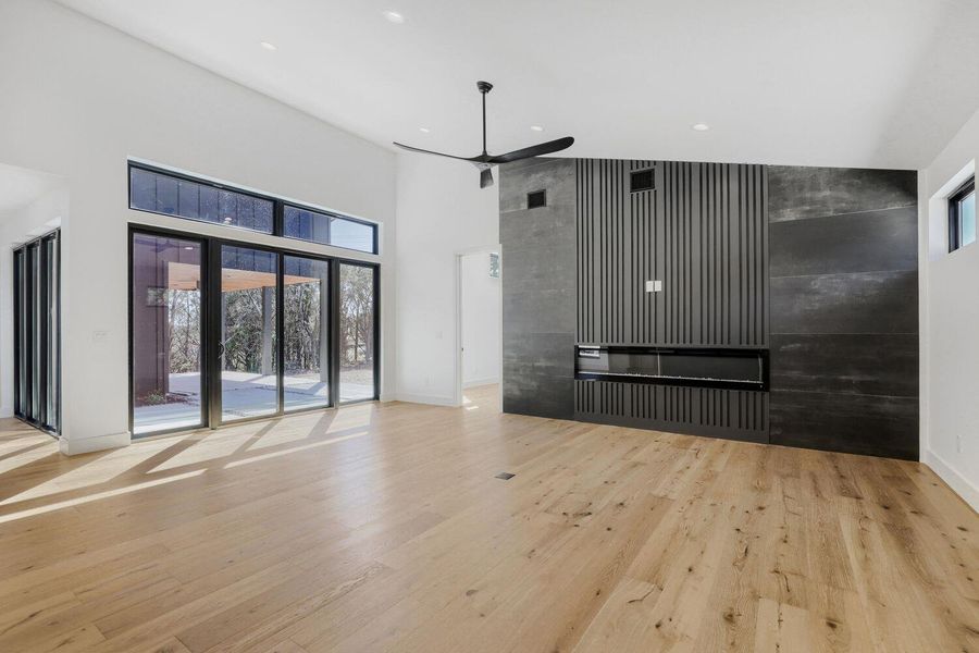 Unfurnished living room with light wood-type flooring, an accent wall, a high ceiling, recessed lighting, and a ceiling fan Unfurnished living room with light wood-type flooring, an accent wall, a high ceiling, recessed lighting, and a ceiling fan