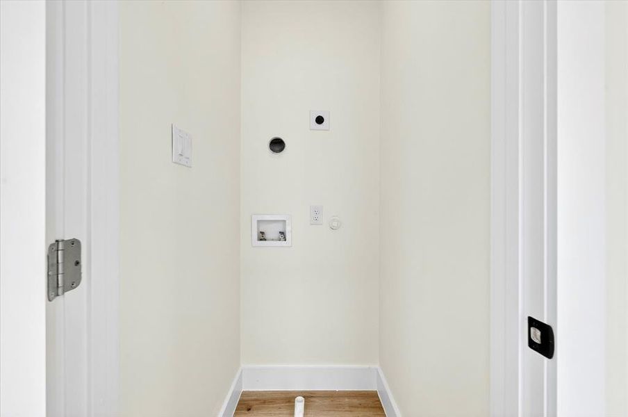 Dedicated laundry area featuring a light-toned wall finish, white baseboards, and wood-finish flooring