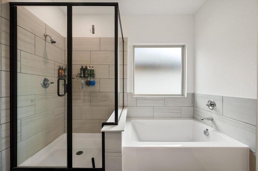 Modern bathroom featuring a walk-in shower with black-framed glass enclosure, white tile surround, and a built-in bathtub with a frosted window