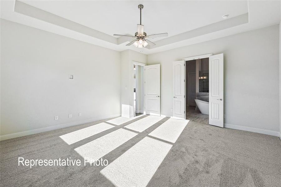 Unfurnished bedroom with ceiling fan, carpet flooring, ensuite bath, and a tray ceiling