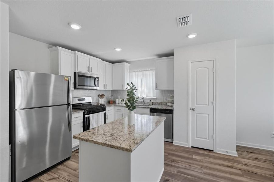 Kitchen featuring appliances with stainless steel finishes, light stone countertops, decorative backsplash, a kitchen island, and white cabinets