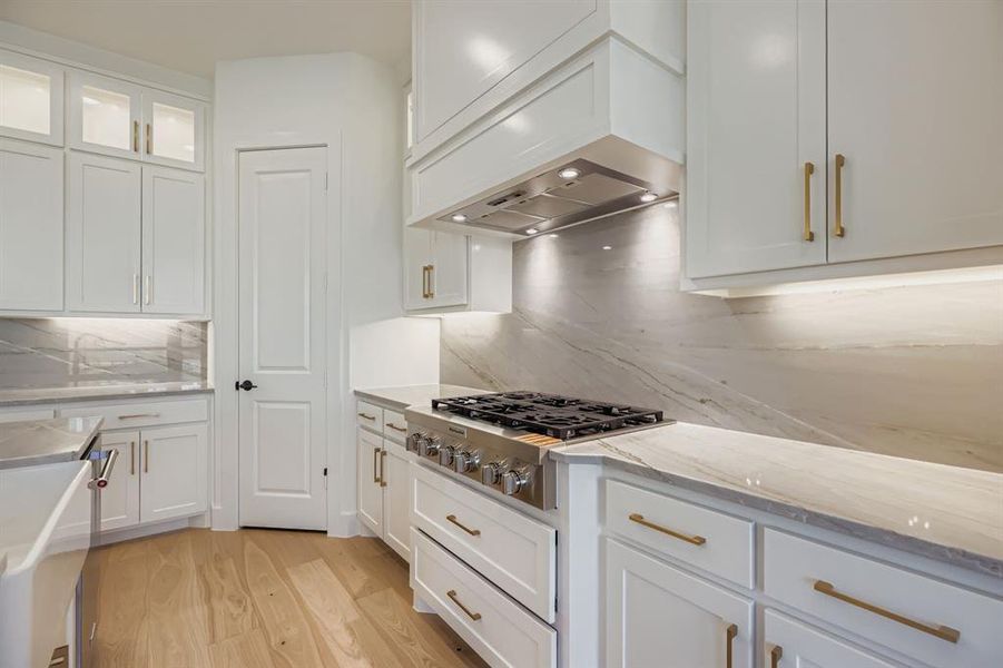 Kitchen with white cabinets, light stone countertops, light wood finished floors, backsplash, and stainless steel appliances Kitchen with white cabinets, light stone countertops, light wood finished floors, backsplash, and stainless steel appliances