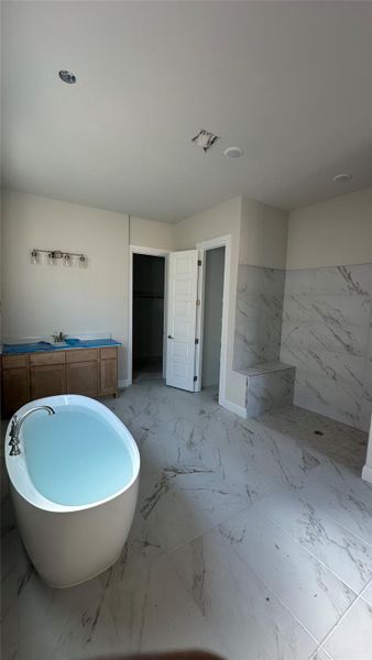 Full bath featuring a freestanding tub, marble finish floors, vanity, wainscoting, and tile walls