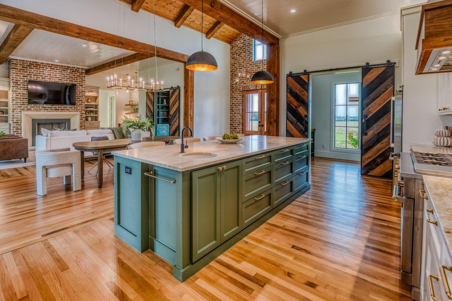Kitchen with a barn door, green cabinetry, open floor plan, light stone counters, and an island with sink Kitchen with a barn door, green cabinetry, open floor plan, light stone counters, and an island with sink