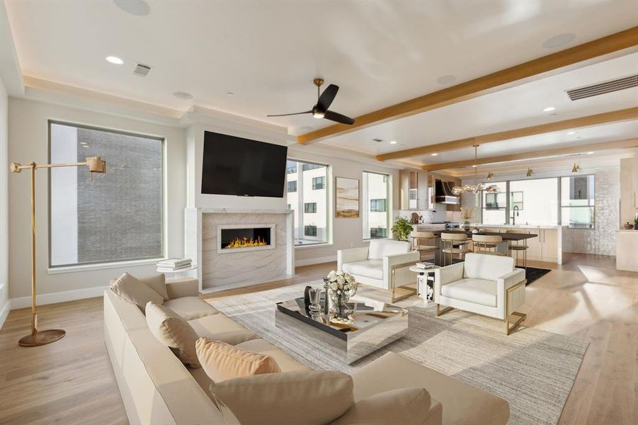 Living area featuring light wood finished floors, a lit fireplace, baseboards, beam ceiling, and a ceiling fan