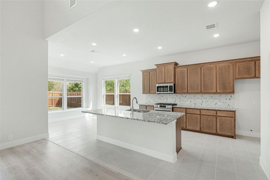 Kitchen with large island, granite countertops, brown cabinets, and stainless steel appliances