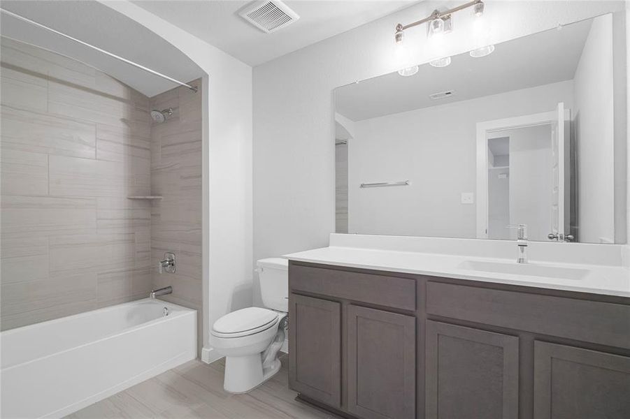 Secondary bathroom features light countertops and stained cabinets, neutral paint, shower/tub combo with tile surround, large mirror, tile floors, sleek fixtures and modern finishes.