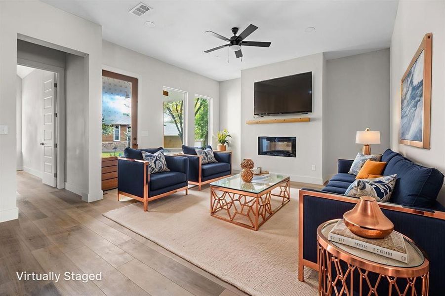 Living room featuring wood finished floors, a glass covered fireplace, and a ceiling fan