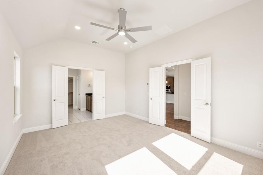 Empty bedroom with carpet, ceiling fan, and two open doors leading to bathroom and hallway Empty bedroom with carpet, ceiling fan, and two open doors leading to bathroom and hallway