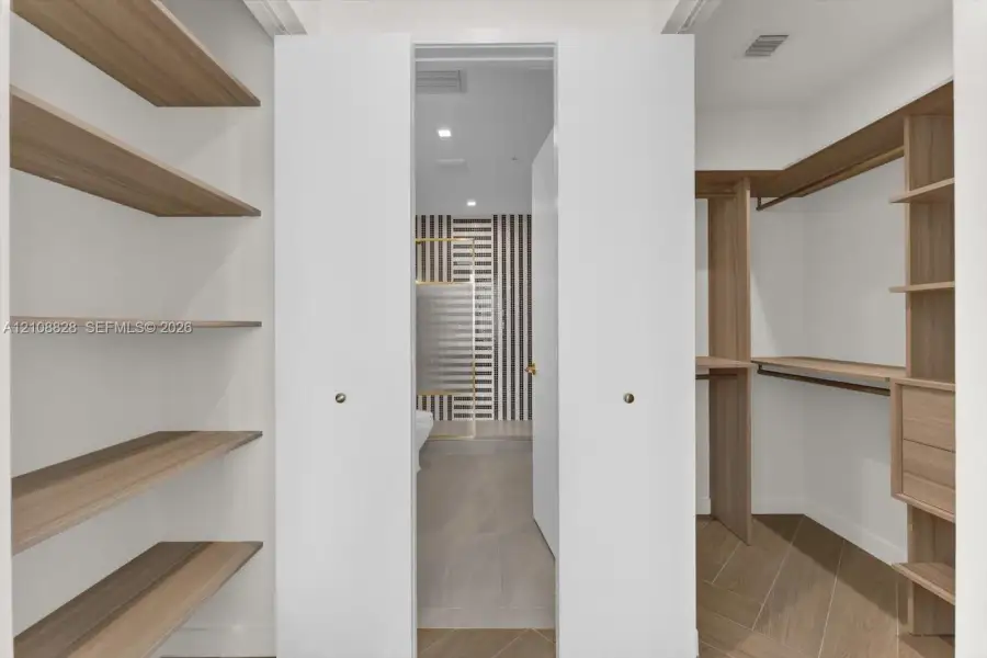 Walk-in closet featuring custom wood-finish built-in shelving, integrated hanging rods, and wood-finish flooring in a herringbone pattern