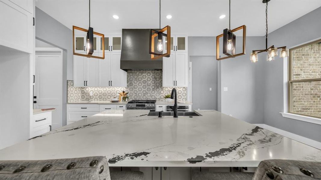 Kitchen featuring white cabinets, light stone countertops, glass insert cabinets, backsplash, and pendant lighting
