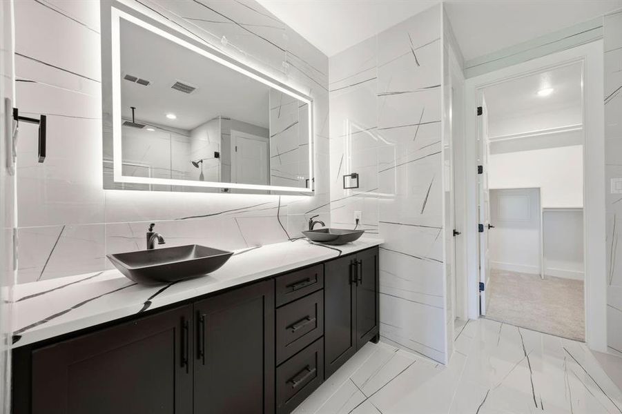 Modern bathroom featuring a double vanity with vessel sinks, dark cabinetry, and a white countertop with black veining Modern bathroom featuring a double vanity with vessel sinks, dark cabinetry, and a white countertop with black veining