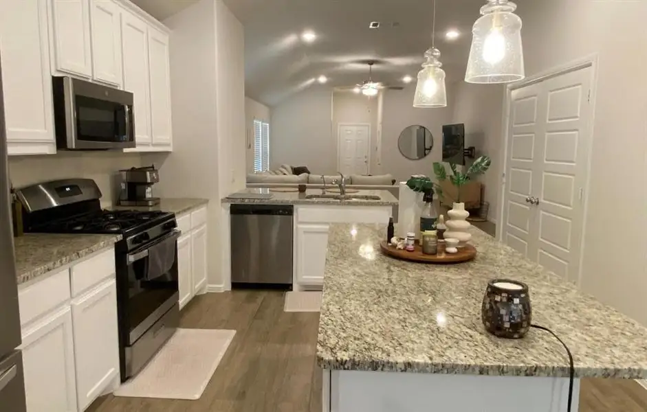 Kitchen with appliances with stainless steel finishes, dark wood-type flooring, pendant lighting, open floor plan, and lofted ceiling Kitchen with appliances with stainless steel finishes, dark wood-type flooring, pendant lighting, open floor plan, and lofted ceiling
