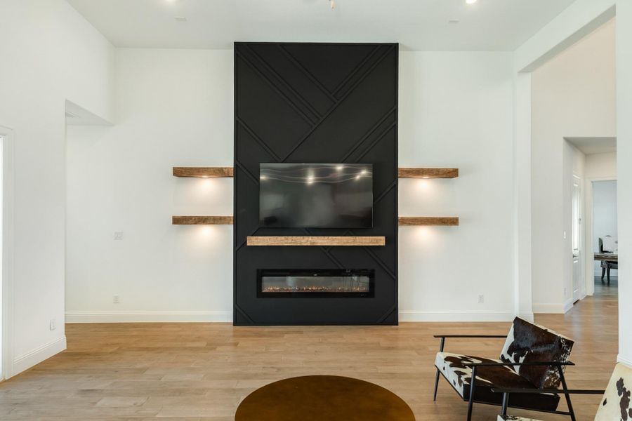Spacious living area featuring a custom fireplace mantel with integrated television mounting space, complemented by seamless transition access to the primary bedroom suite.