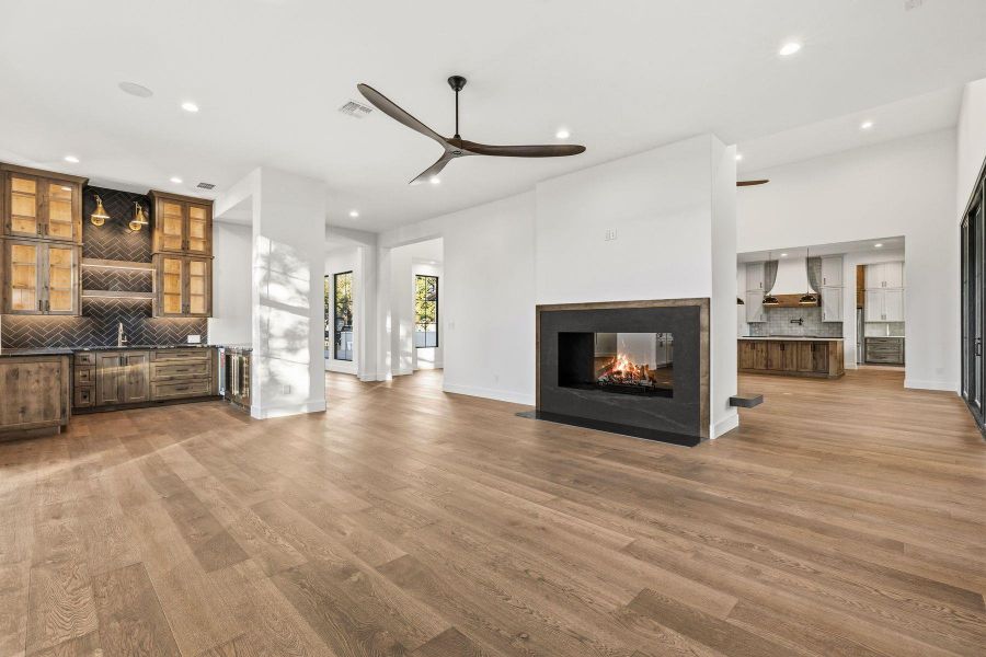 Unfurnished living room with bar area, a multi sided fireplace, ceiling fan, recessed lighting, and light wood finished floors