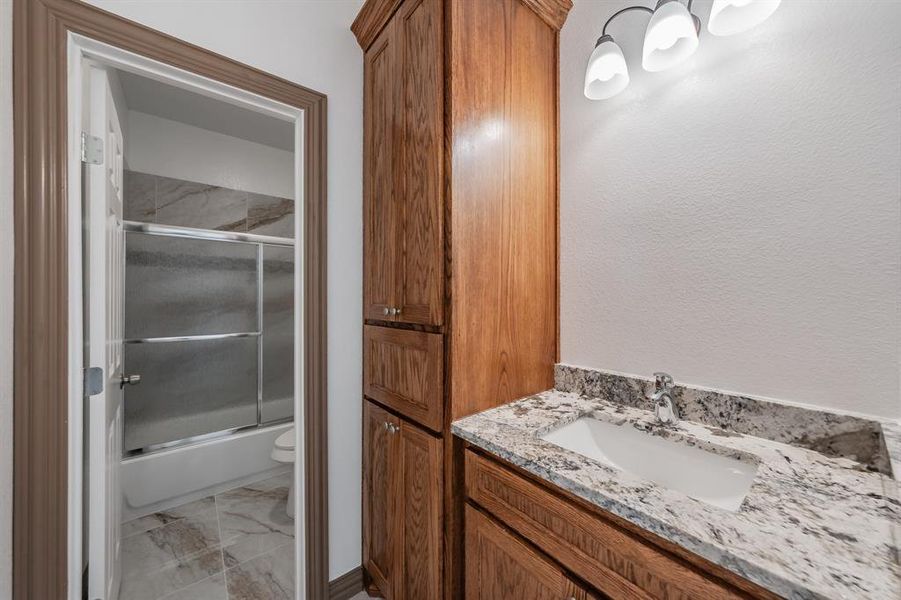 Bathroom with marble finish floor, bath / shower combo with glass door, vanity, and toilet