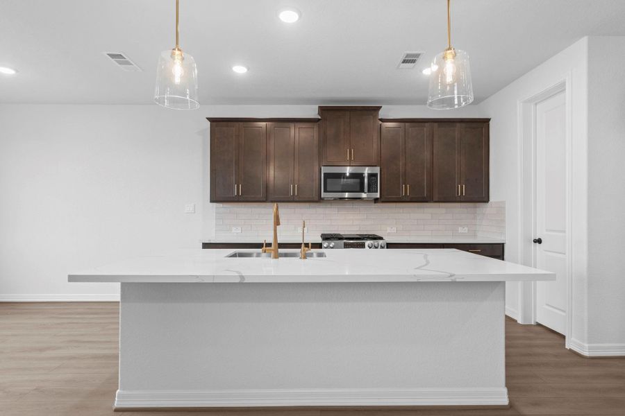 This light and bright kitchen features a large quartz island, white cabinets, a large sink overlooking your family room, recessed lighting, and beautiful backsplash.