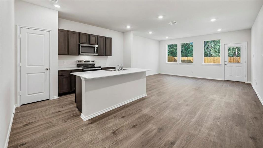 Kitchen with an island with sink, stainless steel appliances, recessed lighting, dark brown cabinets, and light wood finished floors