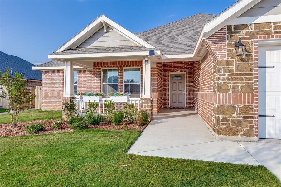 Property entrance with roof with shingles, a lawn, brick siding, and covered porch Property entrance with roof with shingles, a lawn, brick siding, and covered porch