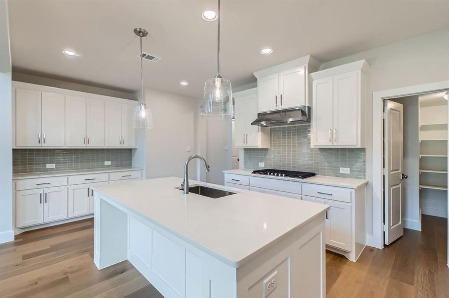 Kitchen featuring under cabinet range hood, light wood-style floors, tasteful backsplash, light countertops, and a center island with sink Kitchen featuring under cabinet range hood, light wood-style floors, tasteful backsplash, light countertops, and a center island with sink