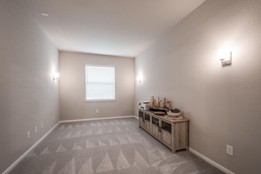 This is a cozy, narrow room with neutral walls and carpet, featuring a window for natural light. Wall sconces provide additional lighting, and there's a wooden sideboard for storage or decor. This is a cozy, narrow room with neutral walls and carpet, featuring a window for natural light. Wall sconces provide additional lighting, and there's a wooden sideboard for storage or decor.