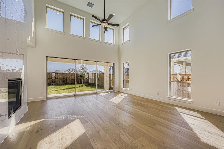 Unfurnished living room featuring a tiled fireplace, light wood-style floors, ceiling fan, and a towering ceiling