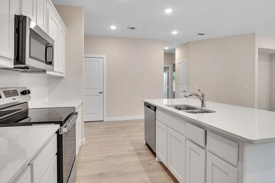 Kitchen featuring appliances with stainless steel finishes, light wood-type flooring, white cabinets, light countertops, and an island with sink Kitchen featuring appliances with stainless steel finishes, light wood-type flooring, white cabinets, light countertops, and an island with sink