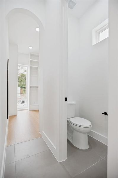 Powder room featuring a single toilet, small frosted window, and large format grey tile flooring