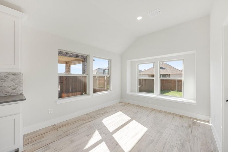 Bright empty dining area with vaulted ceiling, light wood floors, and large windows overlooking backyard fence Bright empty dining area with vaulted ceiling, light wood floors, and large windows overlooking backyard fence