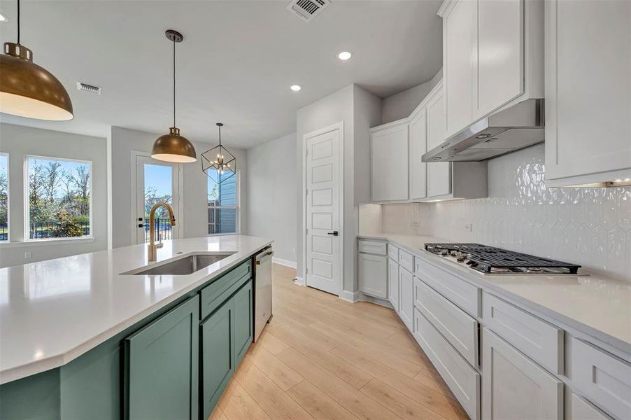 Kitchen featuring backsplash, dual tone cabinetry, light wood-style flooring, decorative light fixtures, and stainless steel appliances Kitchen featuring backsplash, dual tone cabinetry, light wood-style flooring, decorative light fixtures, and stainless steel appliances
