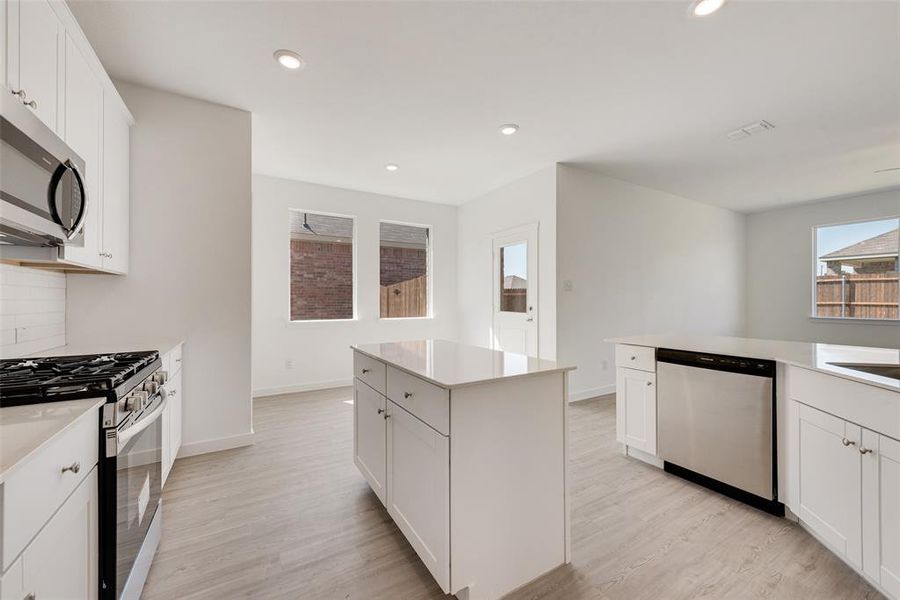 Kitchen with appliances with stainless steel finishes, a center island, light hardwood / wood-style flooring, and white cabinetry