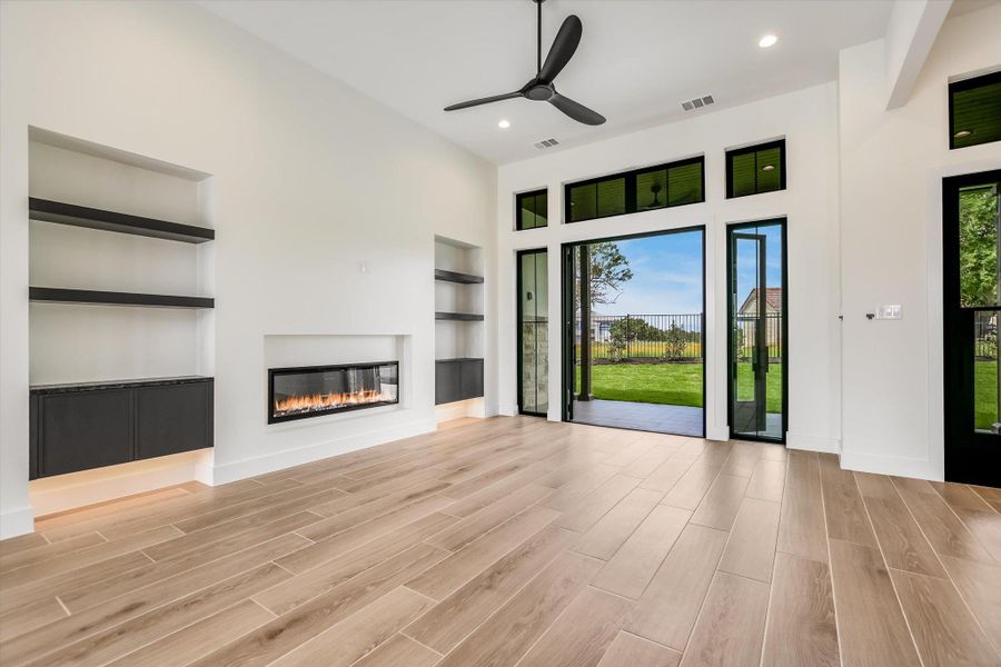 Spacious living area featuring a linear electric fireplace, built-in shelving with lower cabinetry, and wood-finish flooring