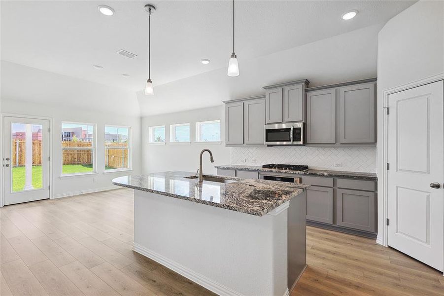 Kitchen featuring light hardwood / wood-style flooring, stainless steel appliances, sink, decorative backsplash, and hanging light fixtures