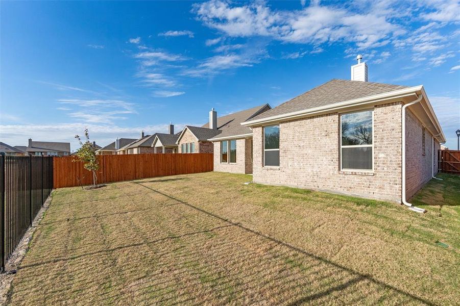 Rear view of house with a fenced backyard, brick siding, a chimney, and a shingled roof