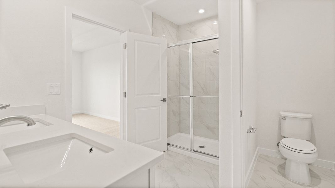 Elegant primary bathroom with glass shower, white vanity, and separate toilet area in the Castaway model