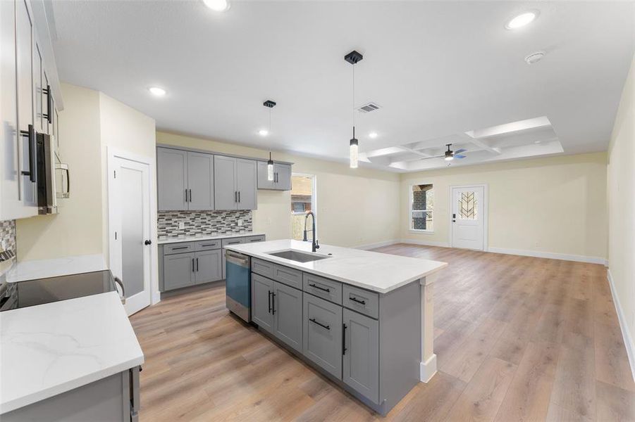 Kitchen with sink, appliances with stainless steel finishes, coffered ceiling, tasteful backsplash, and an island with sink