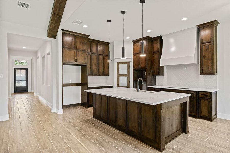 Spacious kitchen featuring dark wood cabinetry, white countertops, and a central island with a sink and pendant lighting