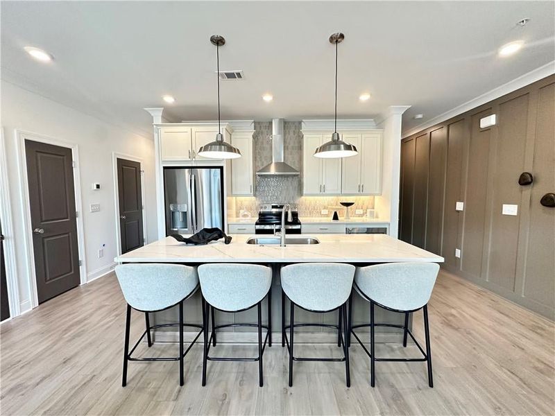 Kitchen featuring a breakfast bar area, wall chimney exhaust hood, a sink, and GE Profile appliances with stainless steel finishes *Photos Showcase Warm Wheat Design Collection from a different Staged Model Home Site*