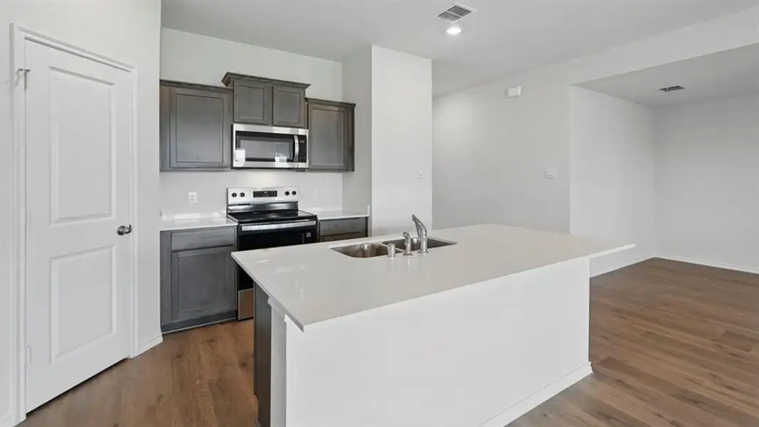 Kitchen featuring a center island with a stainless steel sink and faucet, white countertops, dark wood-finish cabinetry, and stainless steel appliances