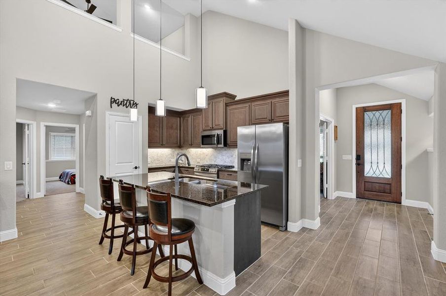 Kitchen featuring wood-finish flooring, dark wood cabinetry, stainless steel appliances, and a central island with a dark countertop and pendant lighting Kitchen featuring wood-finish flooring, dark wood cabinetry, stainless steel appliances, and a central island with a dark countertop and pendant lighting