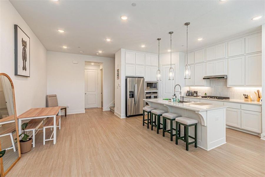 Kitchen featuring a breakfast bar area, white cabinetry, a center island with sink, light wood-type flooring, and stainless steel appliances
