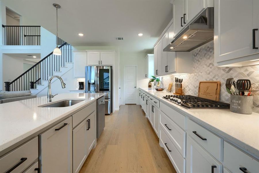 Kitchen featuring light hardwood / wood-style floors, hanging light fixtures, white cabinets, backsplash, and sink