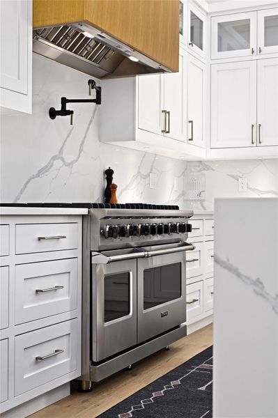 Kitchen with ventilation hood, double oven range, tasteful backsplash, and white cabinets