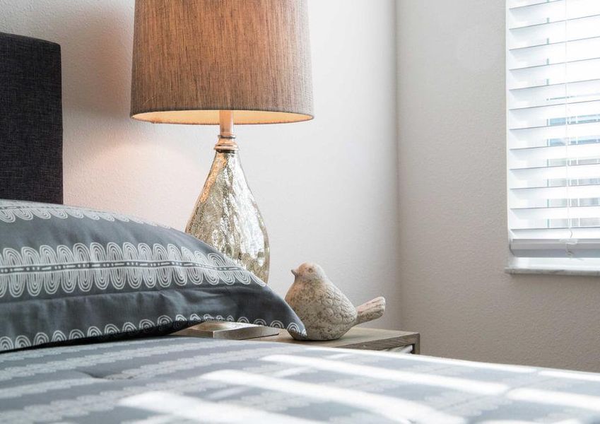 Bedroom completed with patterned beddings, dark wood headboard and shiny lamp with beige shade.